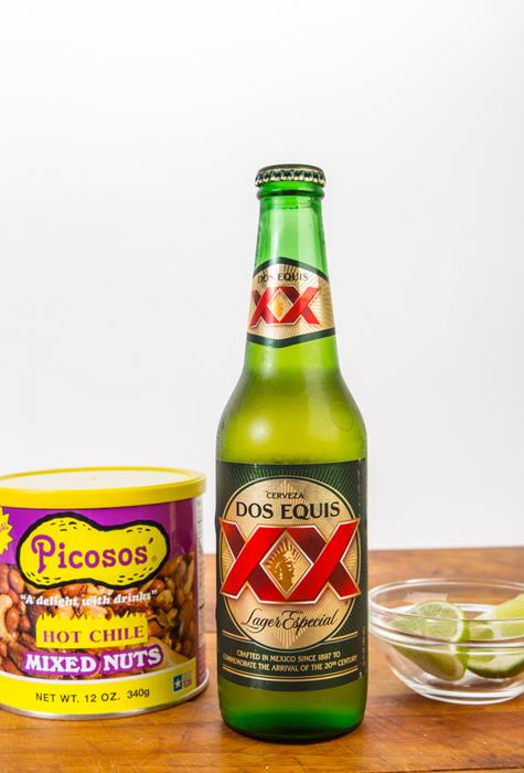 A bottle of Dos Equis beer with mixed nuts and slices of lime
