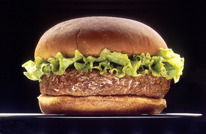 A hamburger with a rim of lettuce sitting on a black plate against a black background