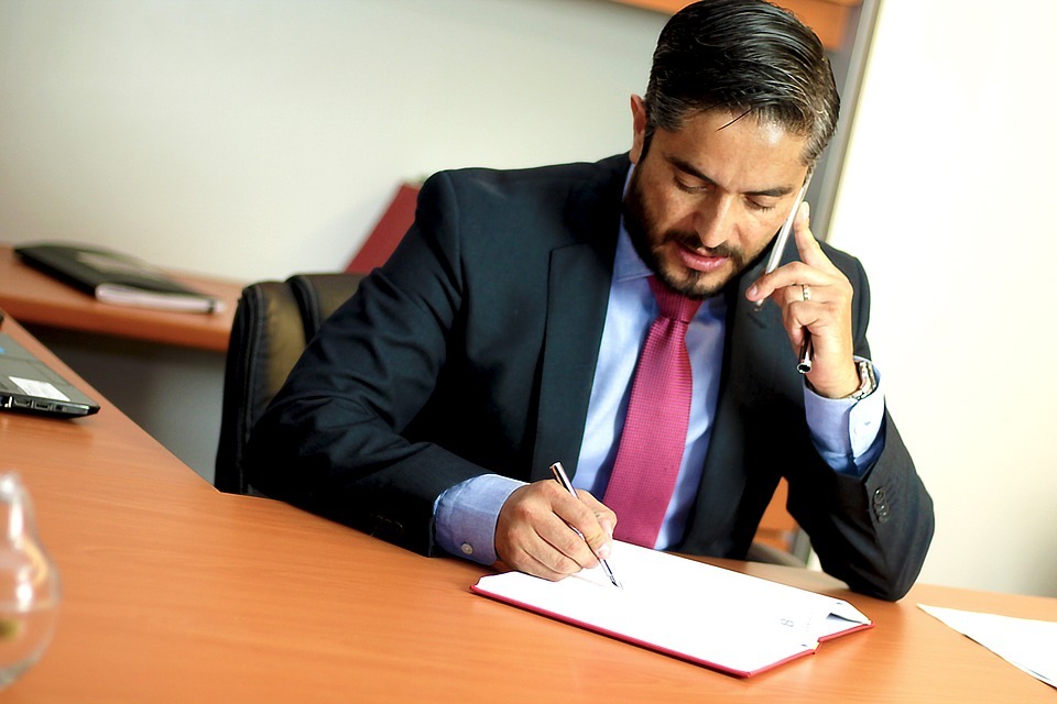 A lawyer at his office desk, scribbling with one hand and holding a phone to his ear on the other hand