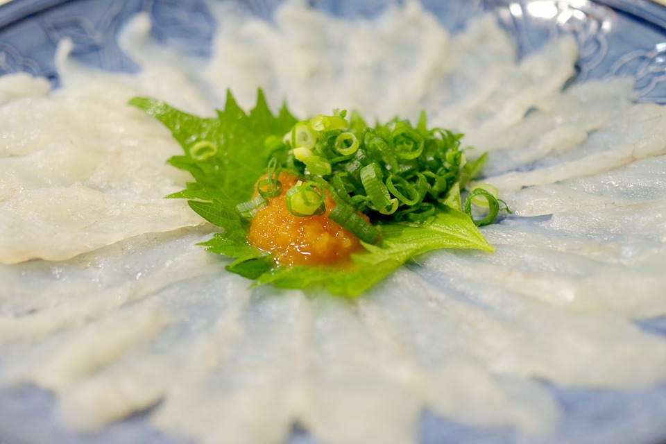 Thin pufferfish strips served on a plate and garnished with greens