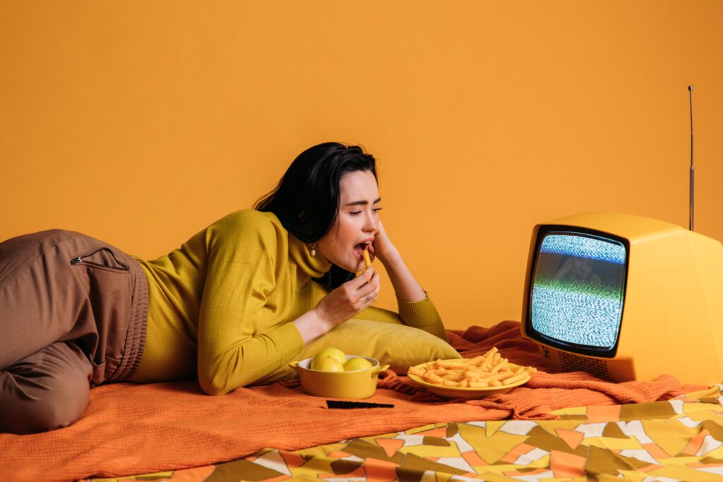 woman in yellow long sleeve shirt watching tv and eating image