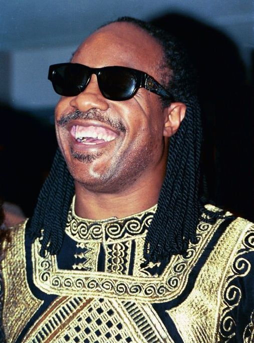Stevie Wonder wearing sunglasses and a black and gold shirt image