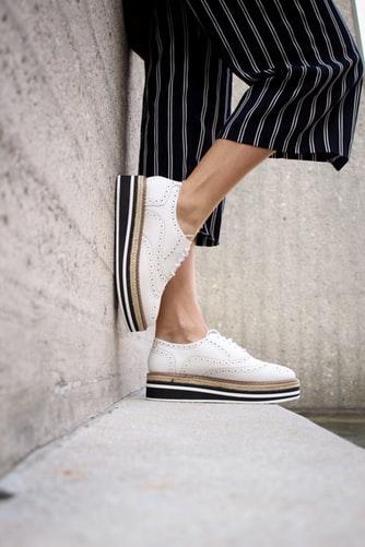 woman wearing white platform shoes with black and white striped poants