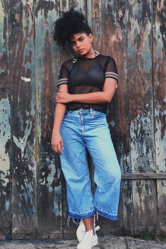 woman wearing wide legged jeans with black shirt posing in front of a wooden wall