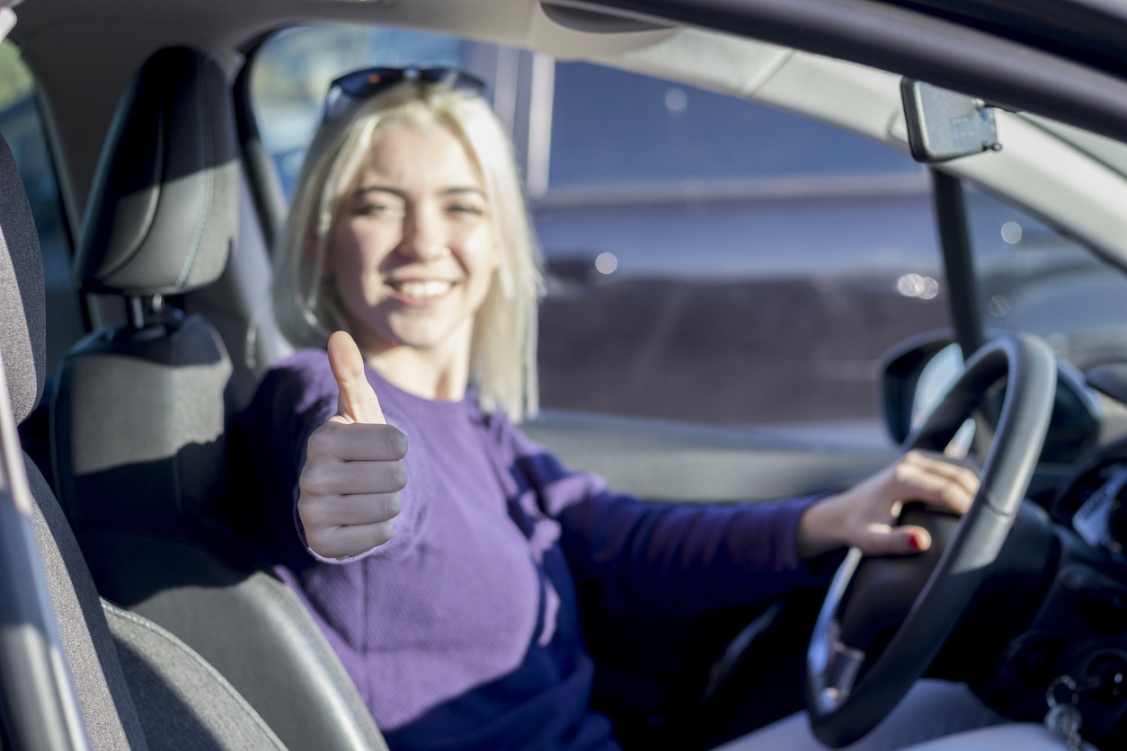 Beautiful woman inside a car driving in the street and gesturing thumb up