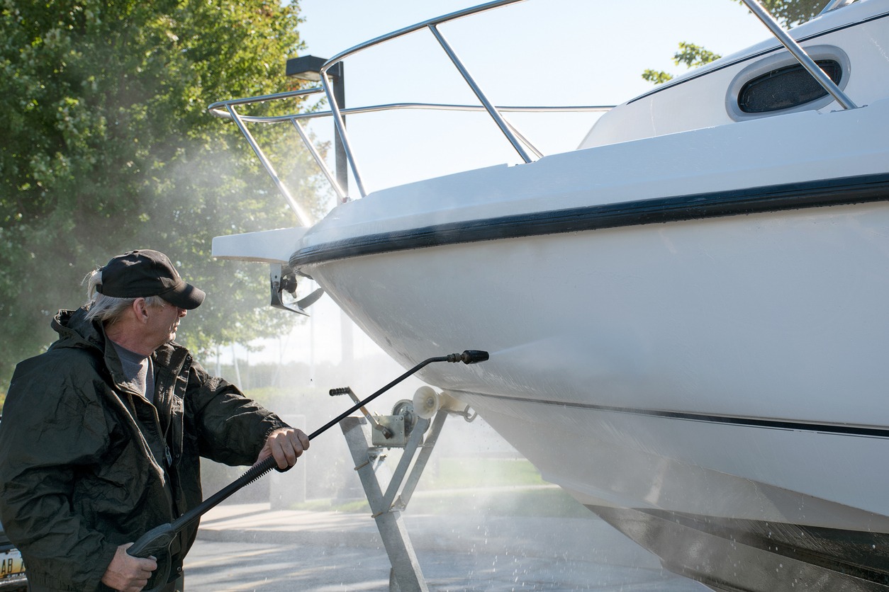 Caucasian man using a pressure washer to clean boat hull
