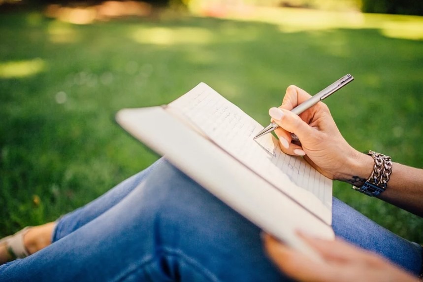 person writing on a notebook outdoors