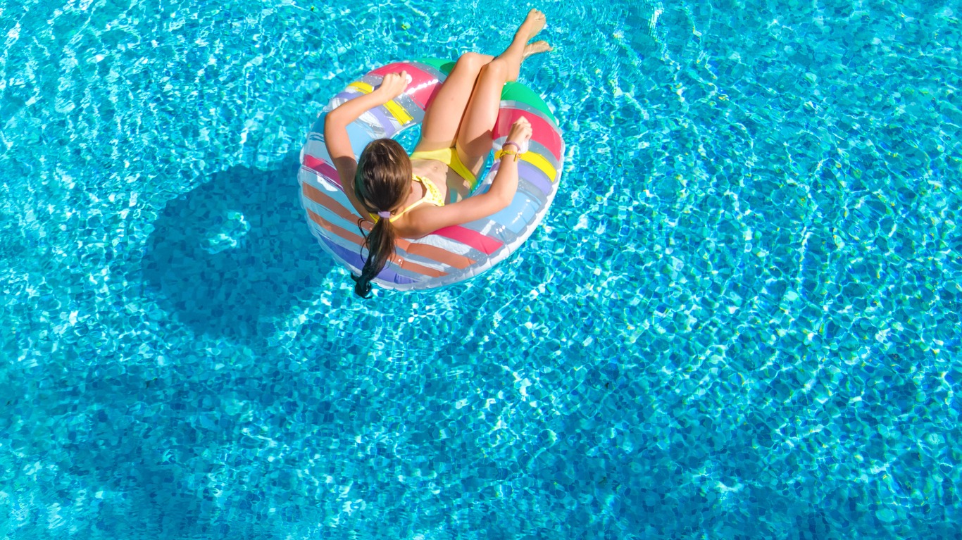 Aerial view of girl in swimming pool from above, kid swims on inflatable ring donut and has fun in water on family vacation