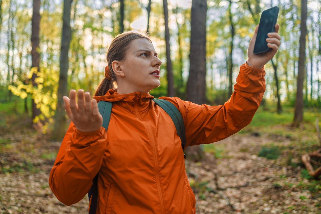 Angry woman tourist hiker hand holding smart phone searching signal in the forest. Communication, cellular problems, bad connection. No signal cellphone network. No communication coverage lost contact signal device.