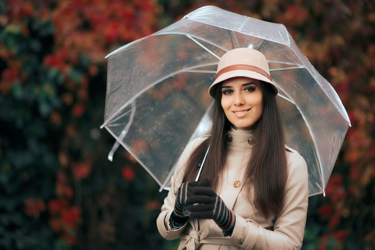 Beautiful girl in a beige trench coat standing outdoors in nature in rainy weather