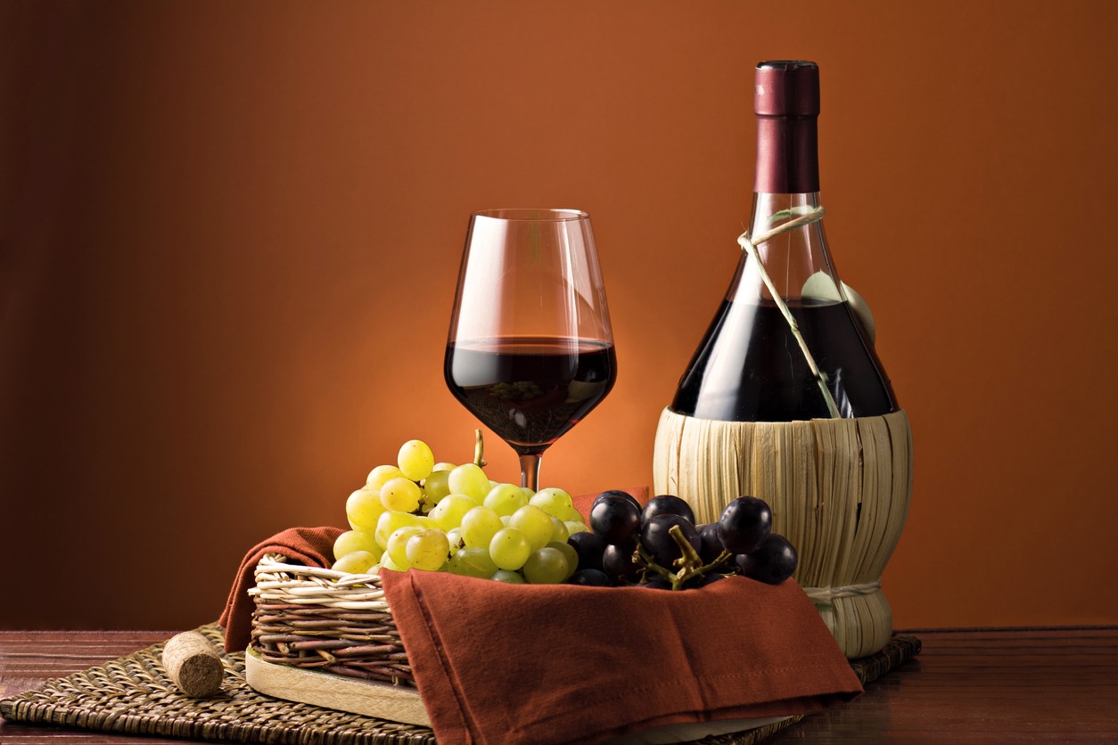 Grape, bottle, and a glass of wine over a wooden table against a light brown background