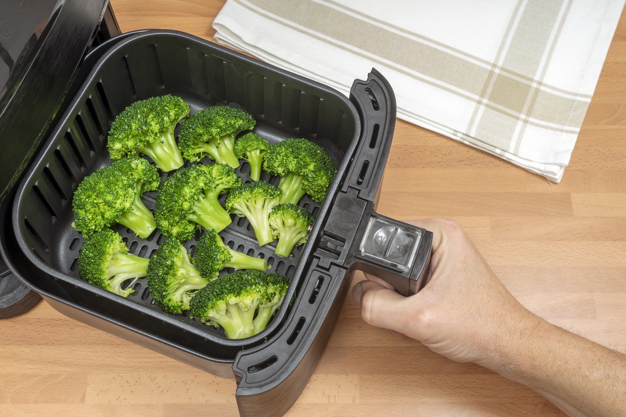 Hand-cooking broccoli florets in an air fryer in the kitchen. Vegan and vegetarian recipes. Keto diet food. Top view