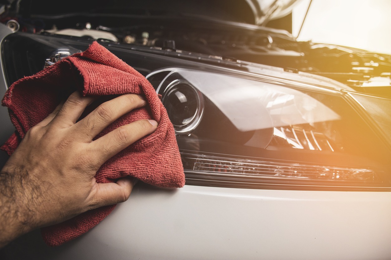 Hand is cleaning car headlight with a red microfiber cloth, Automotive maintenance concept