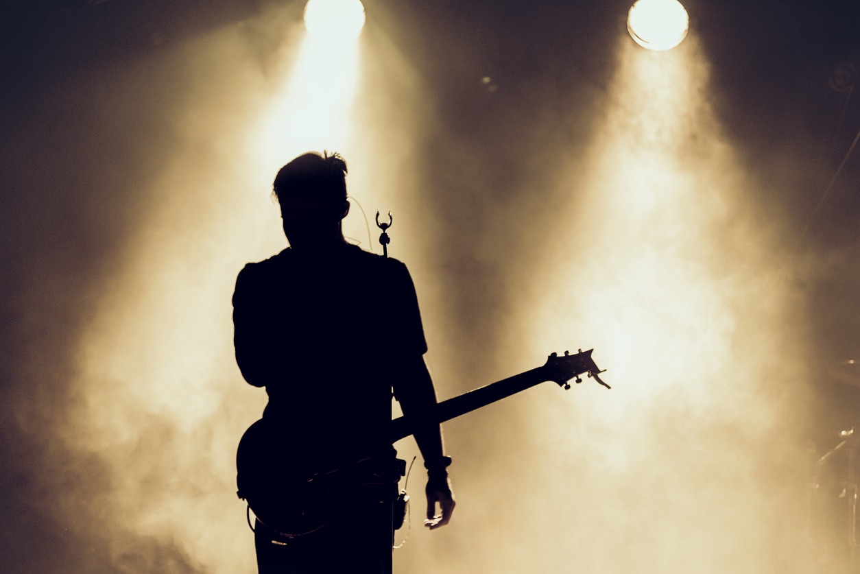 Rock band performs on stage. The guitarist plays solo. Silhouette of a guitar player in action on stage in front of a concert crowd. Smoke. Light