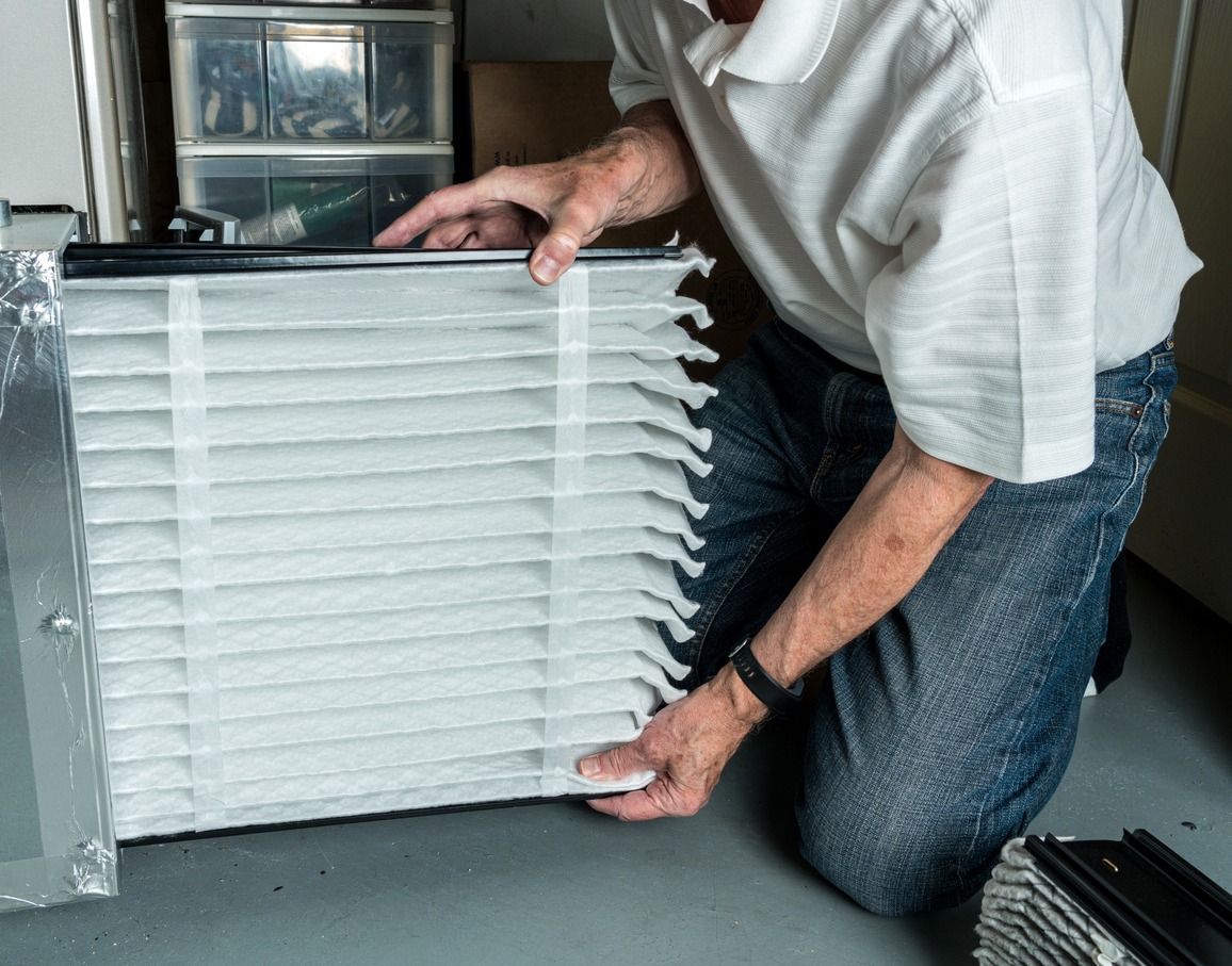 Senior caucasian man checking a clean folded air filter in the HVAC furnace system in the basement of a home