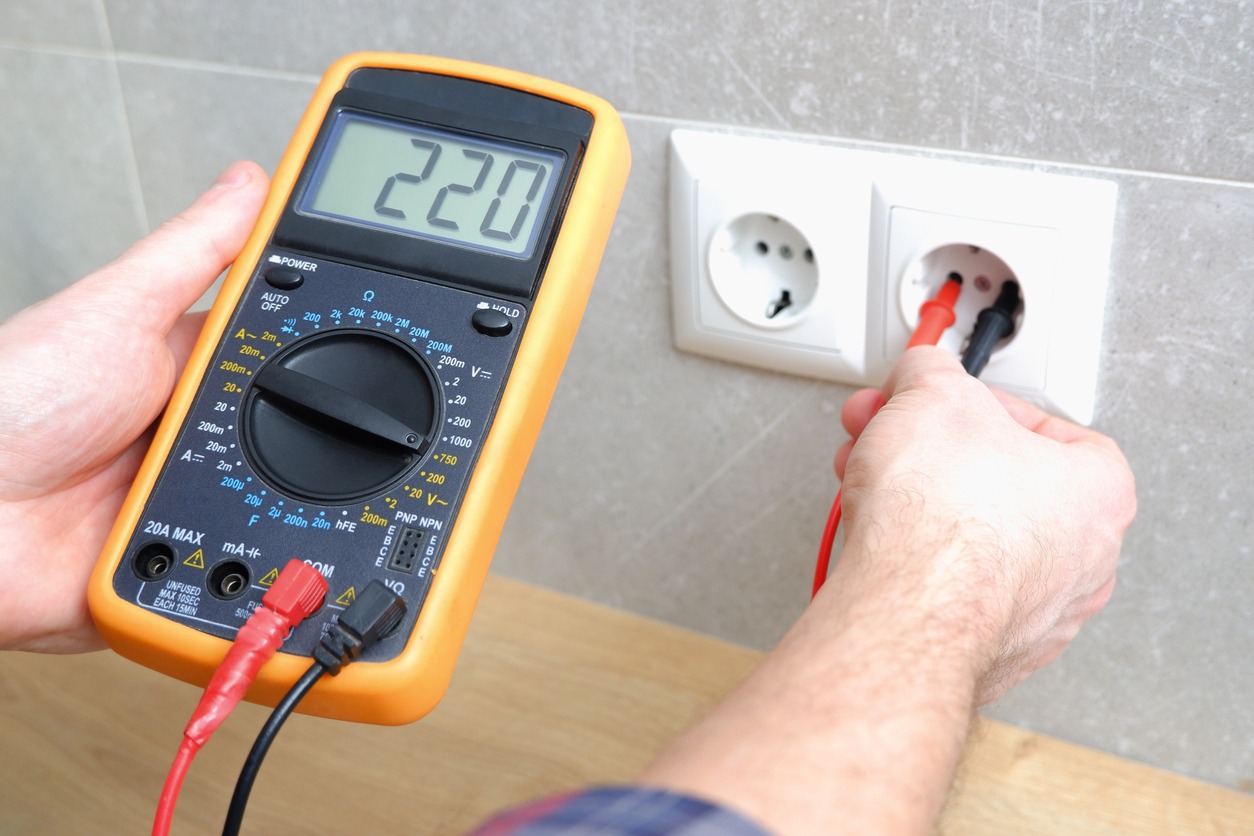 The electrician measures the voltage in the home network by inserting a voltmeter into the outlet. Measurement of voltage in electric networks
