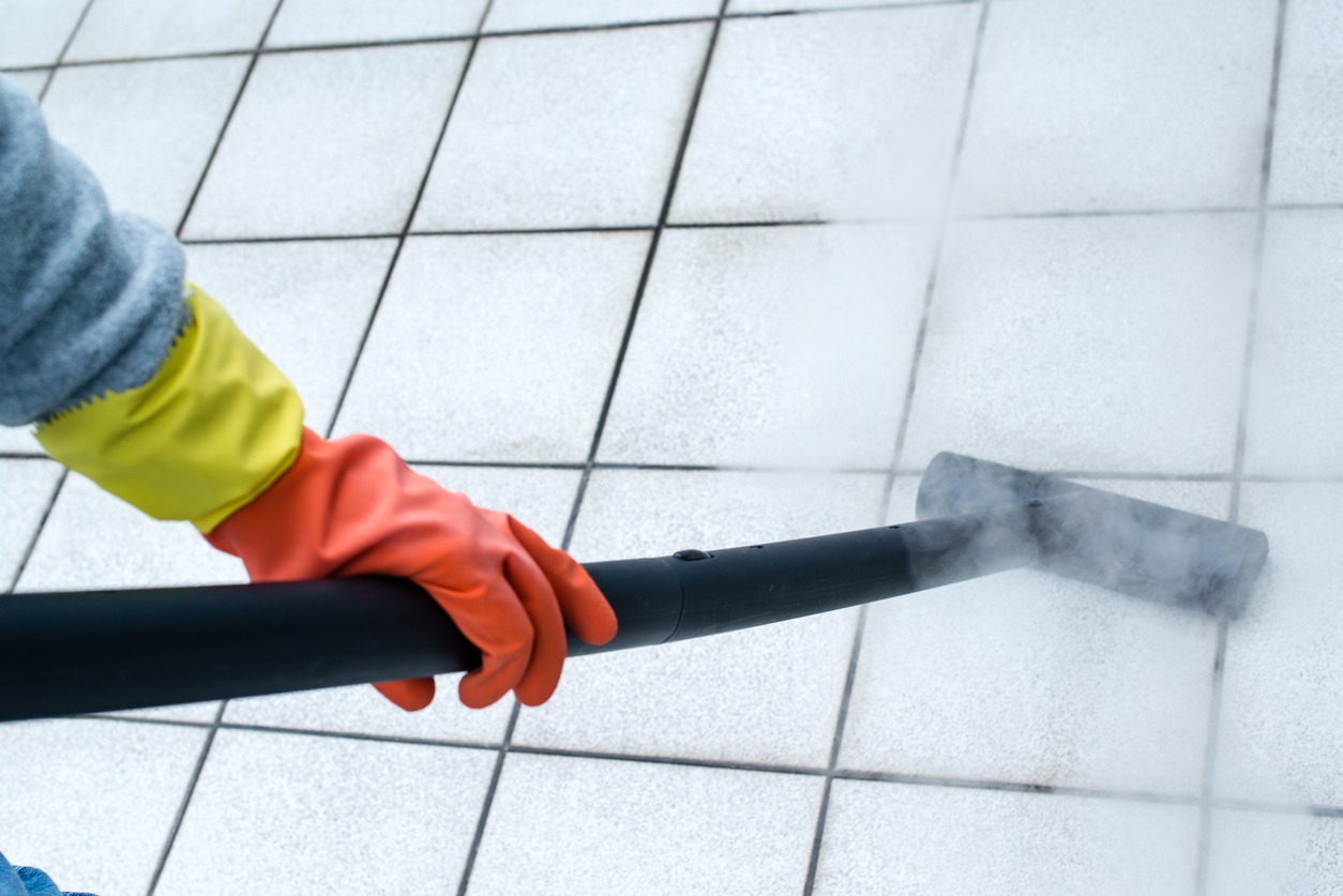 Woman wearing rubber gloves using a steam cleaner to brighten up balcony tiles