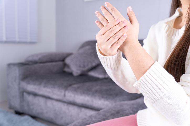 Young woman suffering from hand pain while sitting on the sofa at home. Healthcare medical or daily life concept