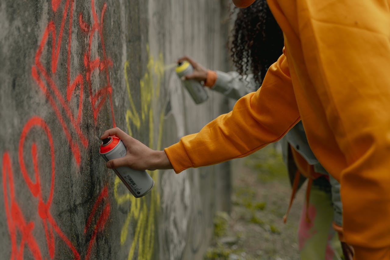 a person in a yellow long-sleeve shirt spray painting a wall