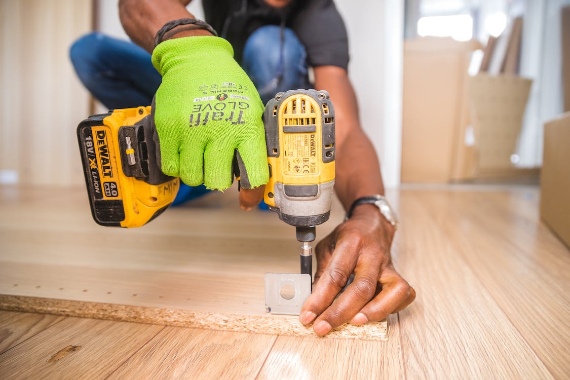 a person using a Dewalt cordless impact driver on brown board