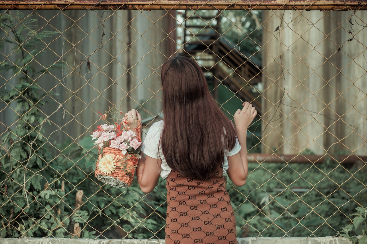 young woman with flowers in basket near fence