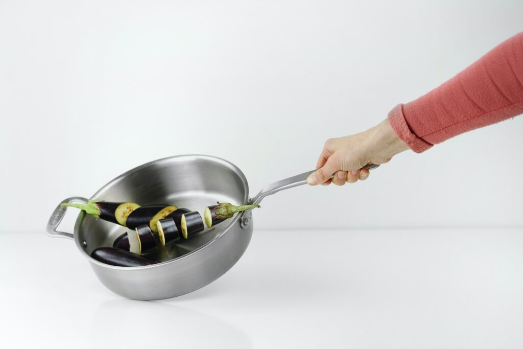 A person holding a stainless steel pan with eggplant in it image