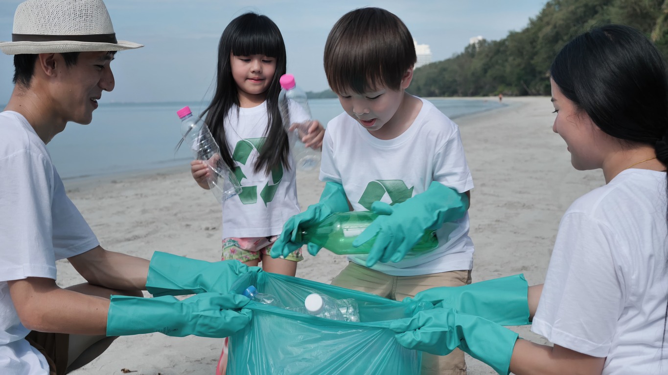 Close-up of Children helping collect the plastic bottles into green plastic bags off the beach. Environmental Conservation Volunteer