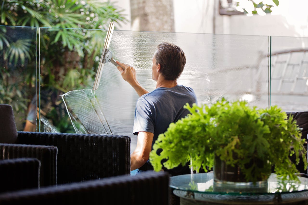 man in gray shirt cleaning transparent glass wall near the sofa