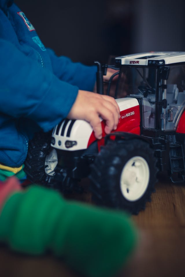person in blue jacket holding red and white tractor toy