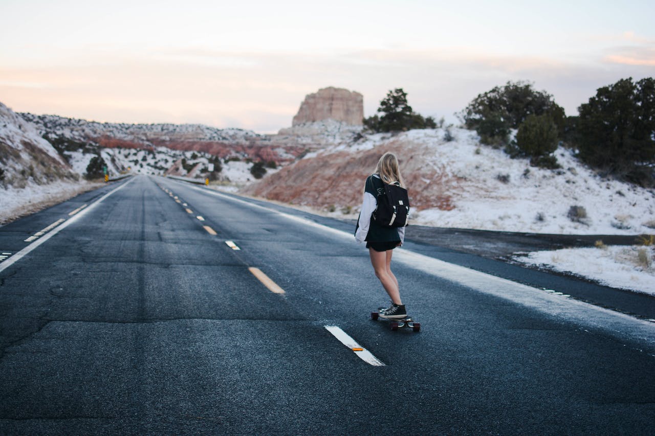 woman in a black and white long-sleeve shirt riding a skateboard on a freeway road