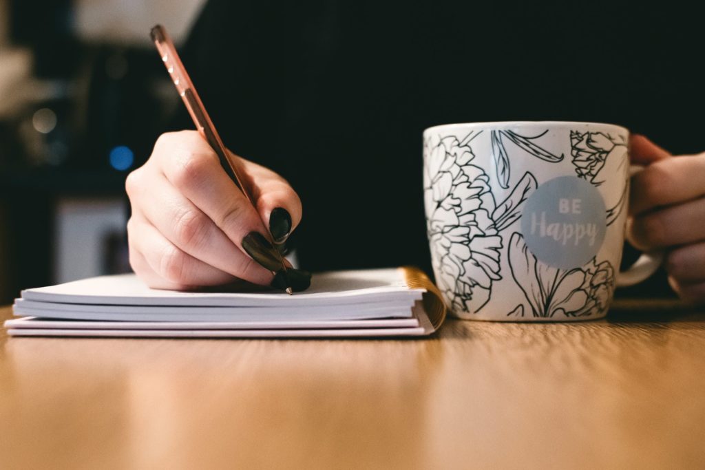 person holding a mug while writing on a notebook