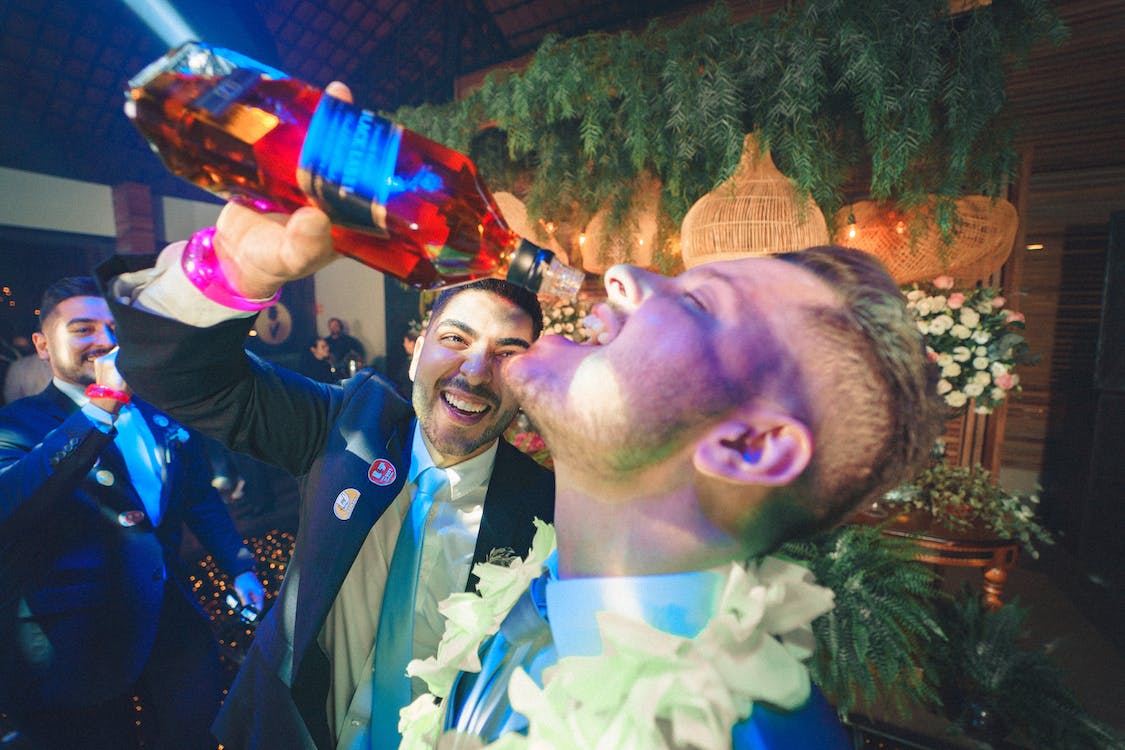 man pouring whiskey from a bottle into another man's mouth