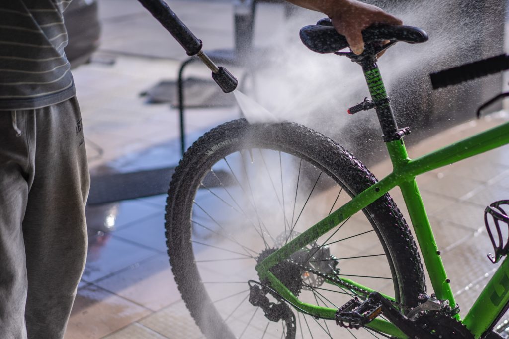 A man washing a green bicycle with a hose