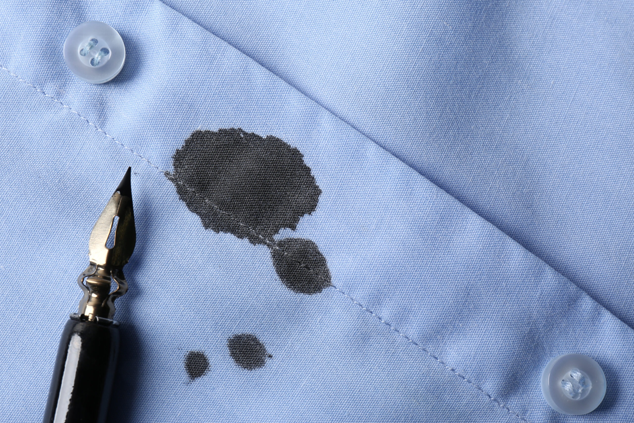 Black ink stain on light blue shirt and pen top view Space for text