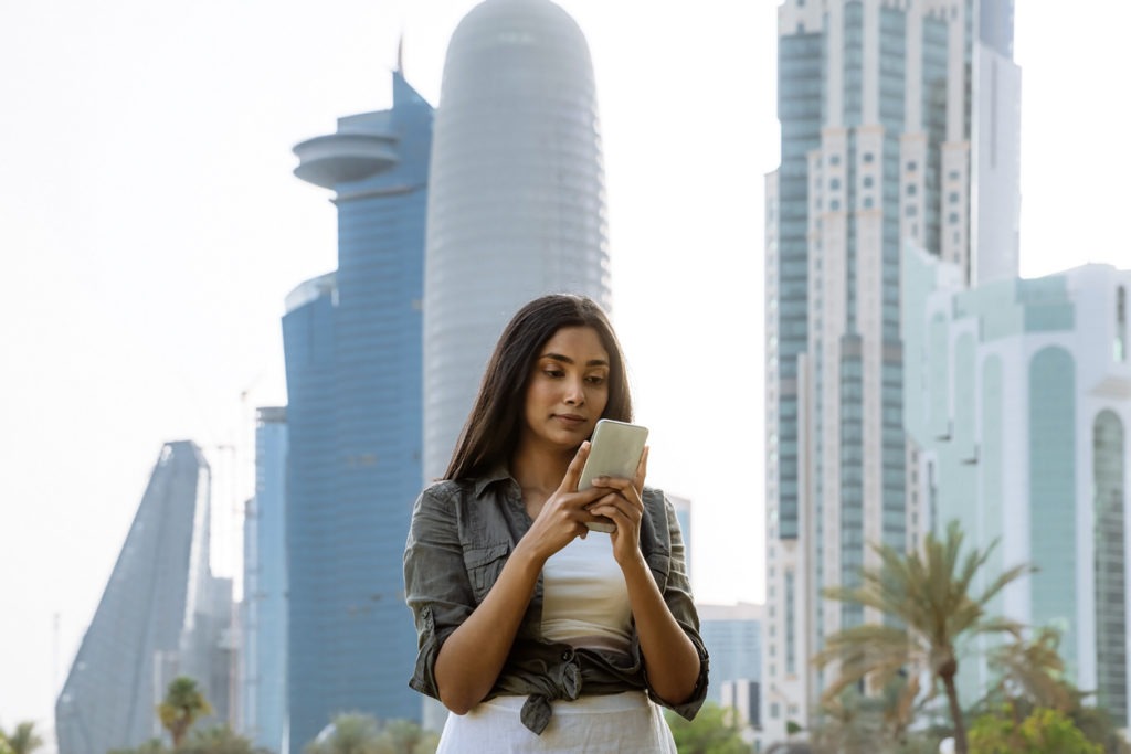Young Indian woman looking at the screen of the smartphone in the downtown Doha, Qatar