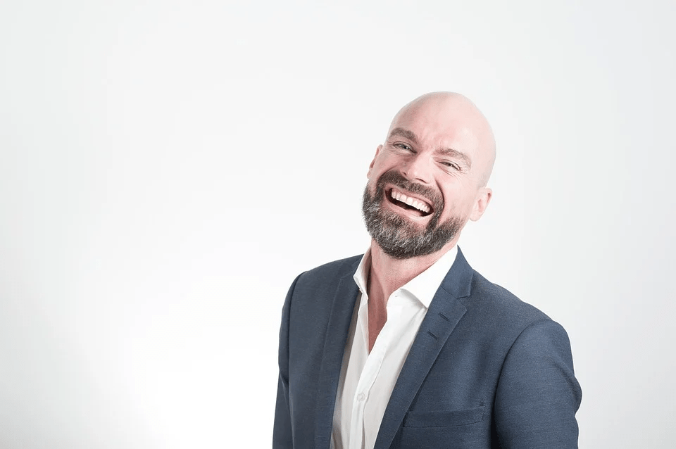 a smiling bald, bearded man in a suit