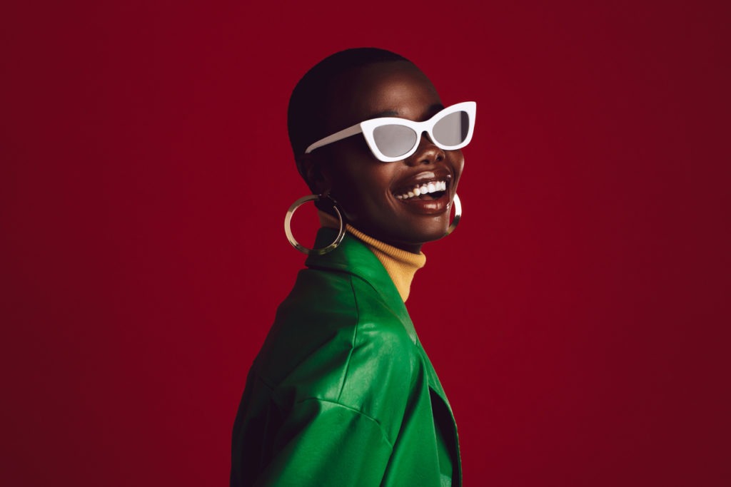 Beautiful woman wearing stylish sunglasses and smiling against red background