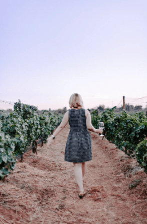 woman holding a glass of wine while walking on a vineyard