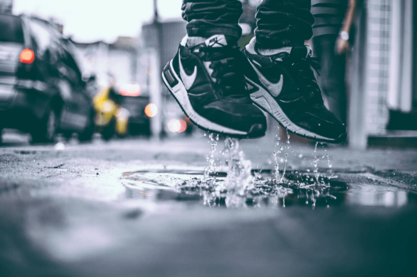feet with black nike shoes jumping over a puddle of water