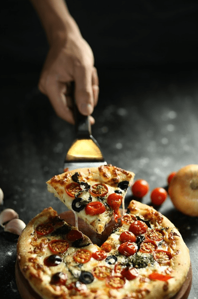 pizza, pizza shovel, a hand taking a pizza slice, cherry tomatoes, garlic cloves, white onion