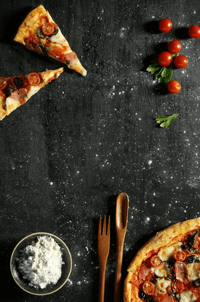 pizza, pizza slice, cherry tomatoes, basil leaves, a bowl of flour, wooden spoon, wooden fork
