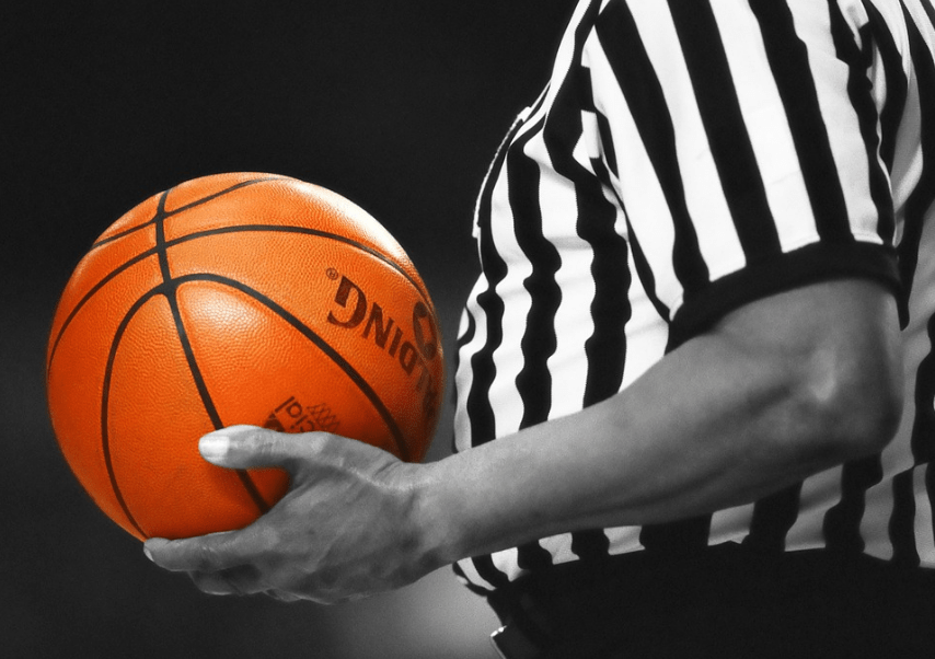 referee dressed in black and white stripes holding an orange Spalding basketball