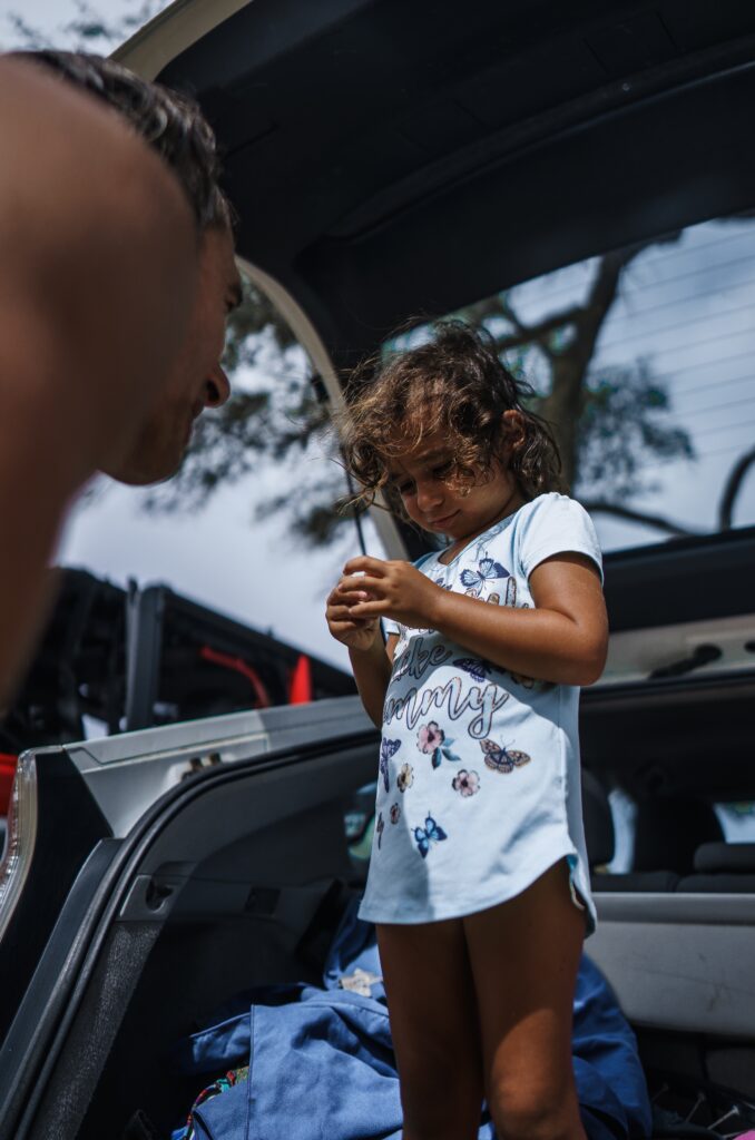 parent talking to a child standing in an opened car trunk image