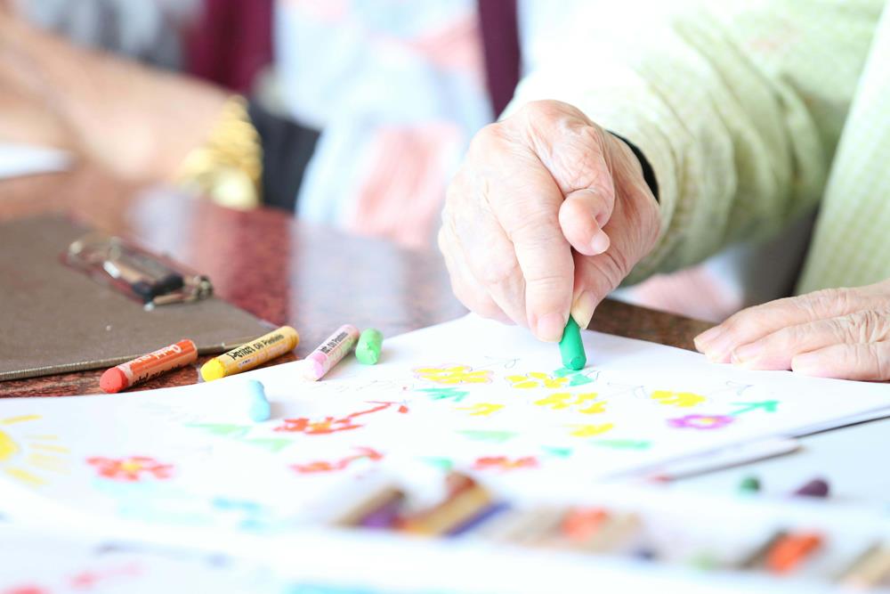 An elderly person drawing using crayons
