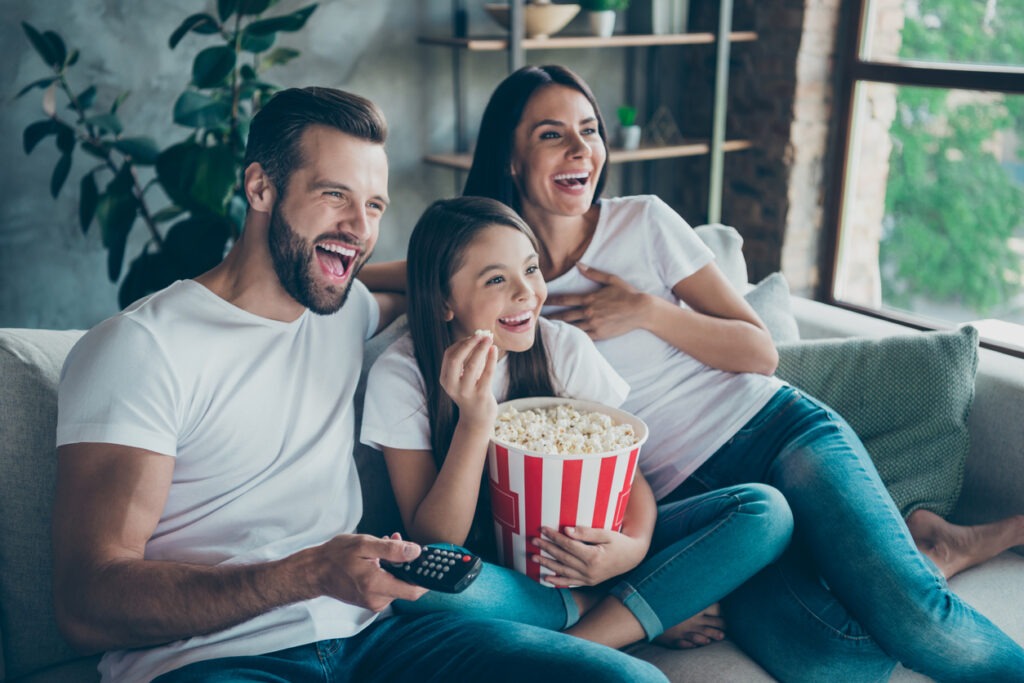 An image of a A family of three laughing and eating popcorn while watching a movie together