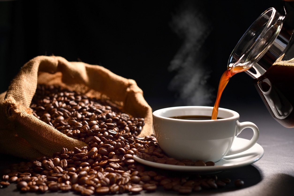 Pouring coffee with smoke on a cup and coffee beans on burlap sack on black background