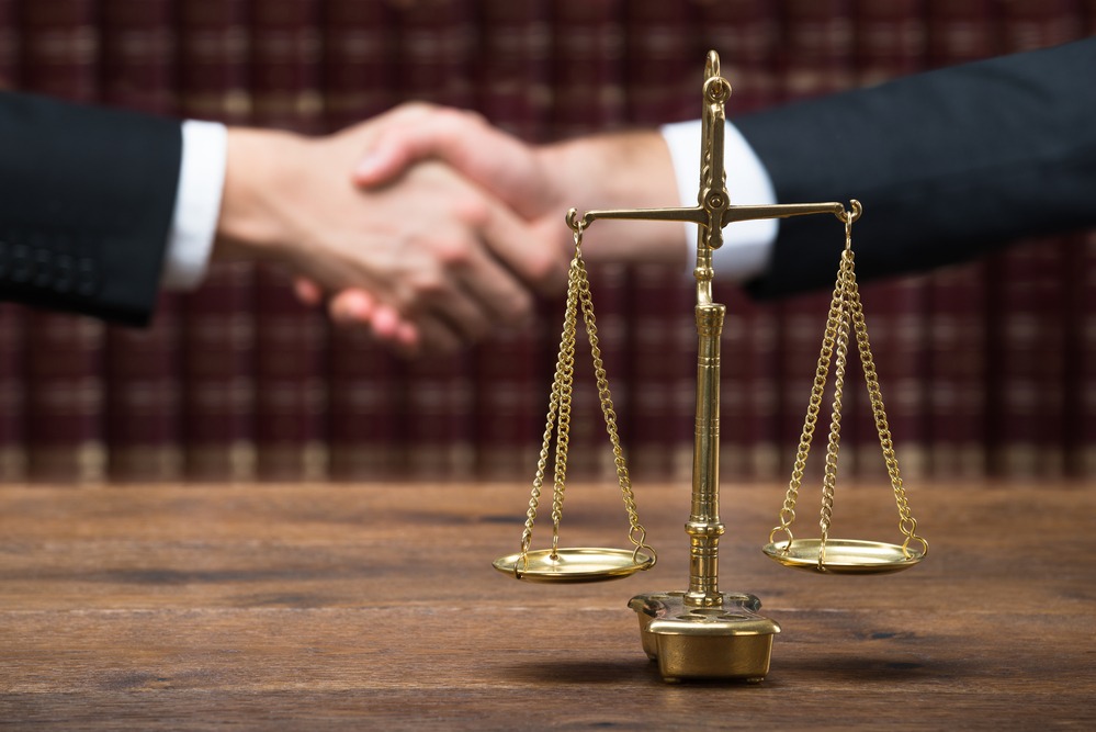 Justice Scale On Table With Judge And Client Shaking Hands