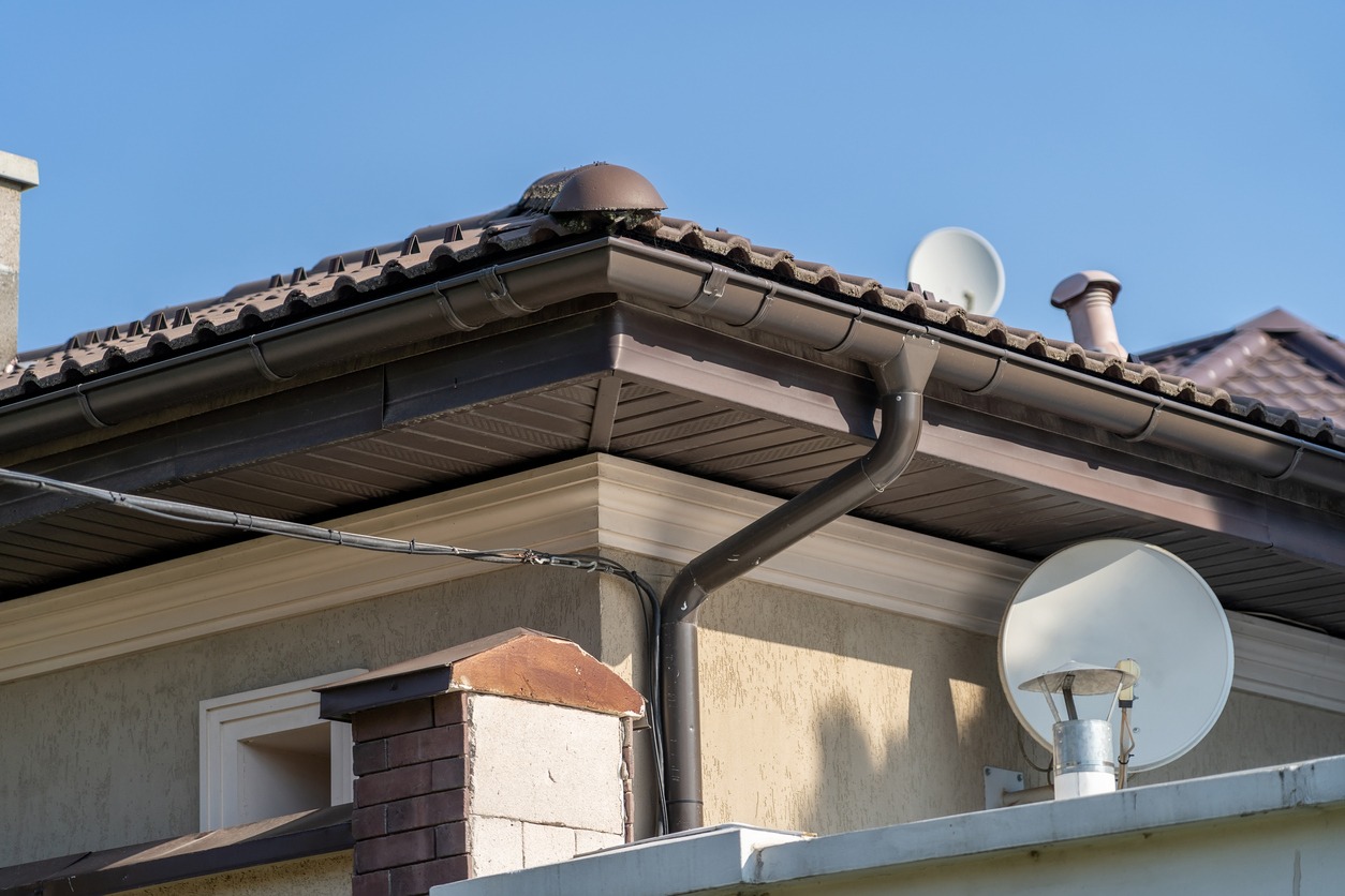 stucco house top with brown gable metal roof, satellite dish and gutter pipe system