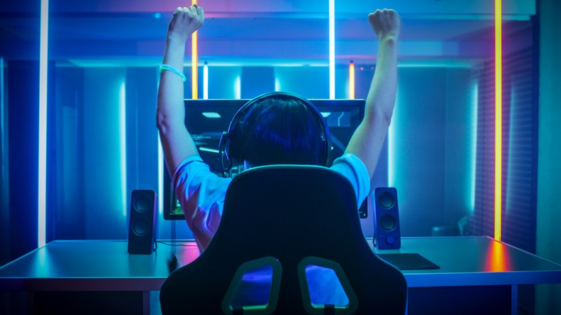 Professional Gamer Playing and Winning in First-Person Shooter Online Video Game on His Personal Computer. Footage Fade out into Bokeh. Room Lit by Neon Lights in Retro Arcade Style. Cyber Sport Championship.