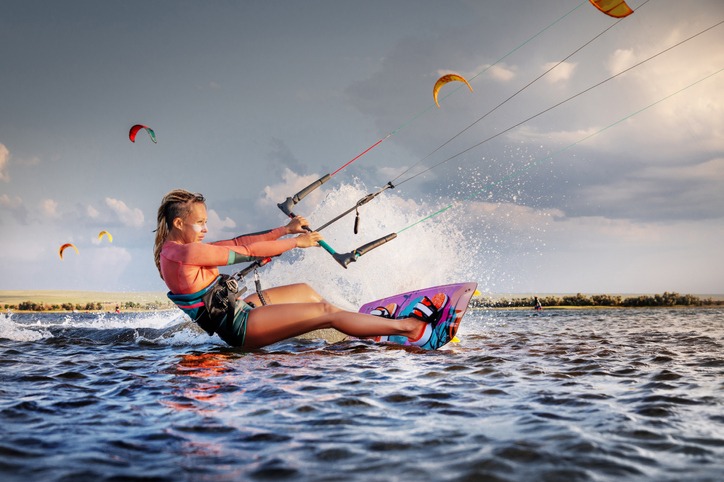 Professional kitesurfer young caucasian woman glides on a board along the sea surface at sunset against the backdrop of beautiful clouds and other kites. Active water sports